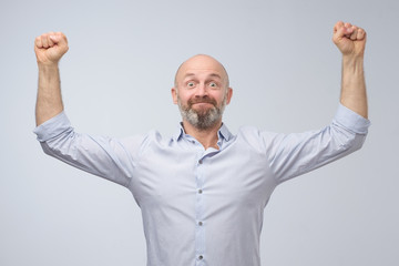 Ecstatic mature man celebrating victory or win against gray background. Positive facial human emotion.