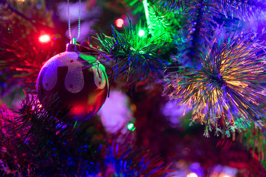 A close up photograph of a Christmas pudding bauble hanging from a green Christmas tree surrounded with multicoloured fairy lights