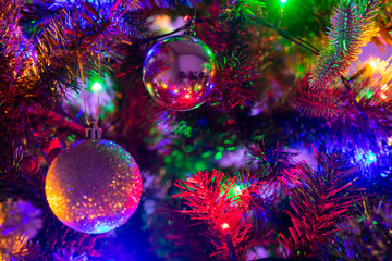 Obraz na płótnie Canvas Multiple glass and glitter Christmas Baubles hanging from a green Christmas tree surrounded by fairy lights