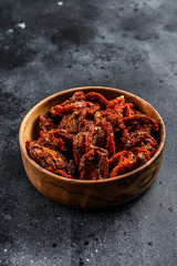 Sun dried tomatoes  in wooden bowl. Black, dark background. Top view