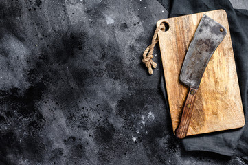 Meat cleaver on old scratched wooden cutting Board. Dark background. Top view. Copy space