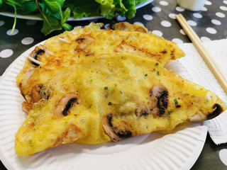 Vietnamese fried pancake made of rice flour, water, and turmeric powder, called "Banh Xeo" served on table with lettuce and various local aromatic herbs