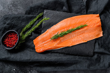 Raw trout fillet with rosemary and pink pepper. Organic fish. Black background. Top view.