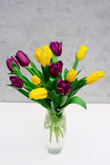 Bouquet of purple and yellow spring tulip flowers in a glass vase on a light background. Mothers Day. International Women's Day.