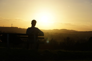 Mann sitzt auf Bank vor Sonnenuntergang