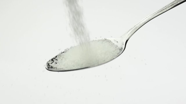 Very beautiful stunning bright white sugar sugar crumbles into a shiny teaspoon
