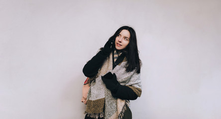 Young woman in autumn coat and wild skarf-wrap talking on mobile phone. Gray background, copy space.