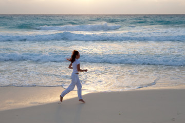 woman jogging on the edge of the sandy beach at sunrise