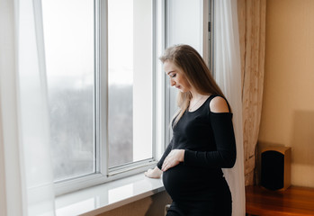 Fototapeta na wymiar A pregnant girl is breathing fresh air from the window