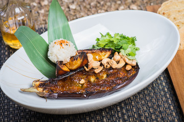 Asian cuisine, baked eggplant with nuts and rice in a deep plate on a table in a restaurant.