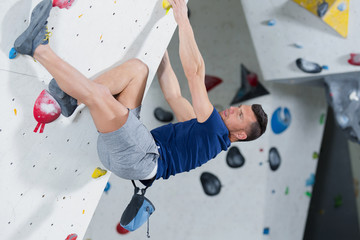 man climber on artificial climbing wall in bouldering gym