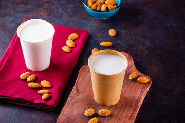Almond milk with almond on dark background. Homemade organic almond milk in a paper cup on a wooden board. Vegan milk from almonds nuts in kraft paper cup. Alternative milk. Zero waste