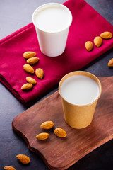 Almond milk with almond on dark background. Homemade organic almond milk in a paper cup on a wooden board. Vegan milk from almonds nuts in kraft paper cup. Alternative milk. Zero waste