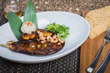 Asian cuisine, baked eggplant with nuts and rice in a deep plate on a table in a restaurant.