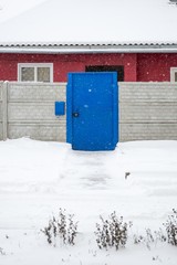 Blue door and concrete fence during a snowfall in winter