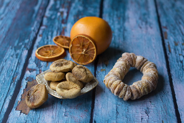 Sun-dried figs on a small plate. A dried fig wreath besprinkled with powdered sugar. A grapefruit and dried orange slices are in a blurry background.