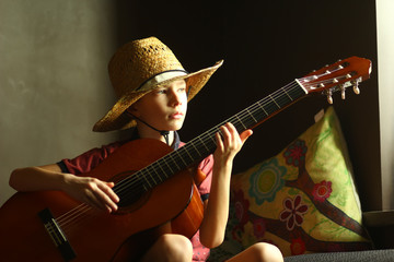 Naklejka premium Portrait of a caucasian boy wearing a straw hat and playing the guitar