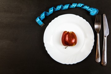 Red apple on a plate with a measuring tape. Weight loss concept. Diet food. Strict diet.