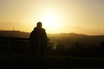 Mann sitzt auf Bank vor Sonnenuntergang