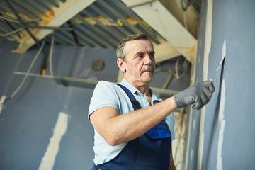 Fototapeta na wymiar Low angle portrait of senior man working on dry wall while renovating house, copy space