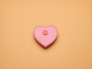 Pink heart figure with button on a beige background with copy space. Valentine's Day.