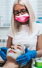 Beautiful young woman receiving facial mask with rejuvenating effects in spa beauty salon.