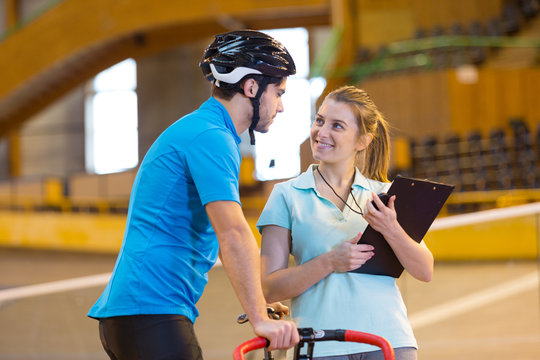 Female Coach Talking To Male Cyclist In Indoor Velodrome