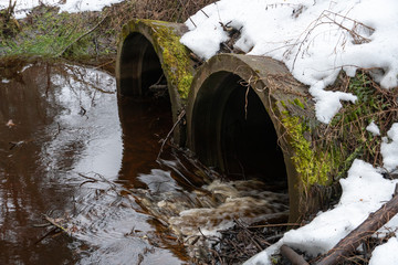 leaky dirty water from large concrete pipes. Snow lies on the pipes. Dirty sewage from the pipe,...