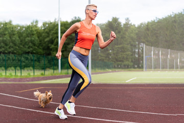 Obraz premium An adult woman runs in the stadium, with a little dog.