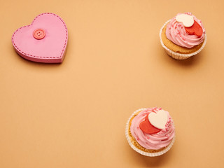Pink heart figure with button and on a beige background with cupcakes cakes copy space.