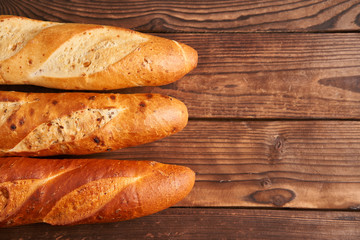 Three crispy french baguettes lie on an old wooden table with free space for text
