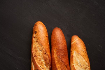 Three crispy french baguettes lie on an old wooden table with free space for text