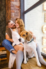 young beautiful couple is sitting at the window with two dogs in a loft apartment