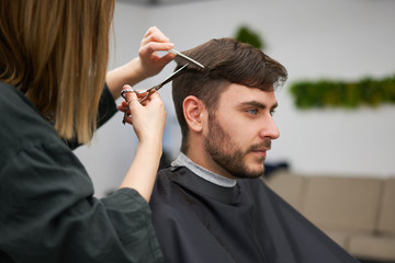 Handsome blue eyed man sitting in barber shop. Hairstylist Hairdresser Woman cutting his hair....