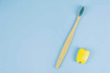 Bamboo wooden brush and dental floss in the form of a tooth on a blue background. Oral care concept. Copyspace