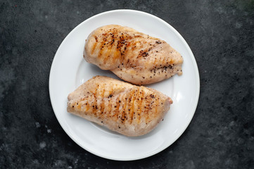 grilled chicken fillet served in a white plate with spices on a stone background