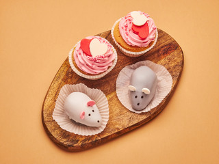 Pink cupcakes, mouse cakes with hearts on a kitchen wooden board on a beige brown background