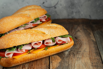 Two Long baguette Sandwiches with arugula, slices of fresh tomatoes, ham and cheese