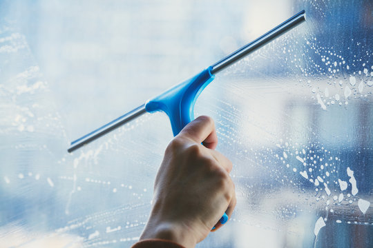 young female hand cleaning dirty glass window with a squeegee