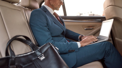 Busy businessman. Cropped photo of a man in full suit working on his laptop while sitting in the car © Svitlana