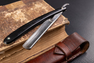 Old sharp razor and book on the table. Accessories for hairdressers and old literature.