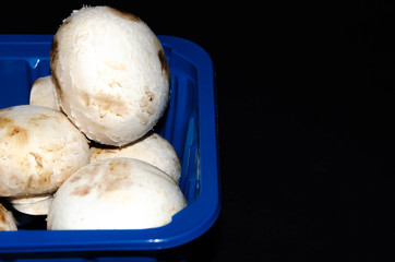 Mushrooms in a blue container from a supermarket. Packaged. Ceps, champignons on a wooden cutting board, on a black background. Bunch of mushrooms  Copy Space