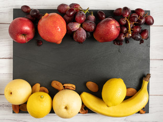 fruits background red and yellow color set on dark stone slake plate and white wood table. Summer abstract creative trendy fresh health concept. Flat lay top view copy space.