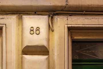 number 86, ancient house number plate on brick wall, Italy
