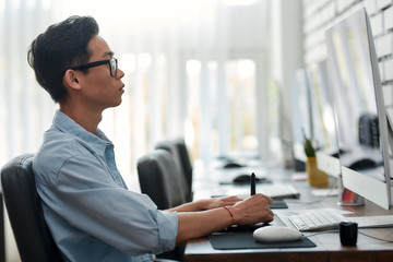 Being creative. Side view of a young asian graphic designer in eyeglasses using digital graphics...