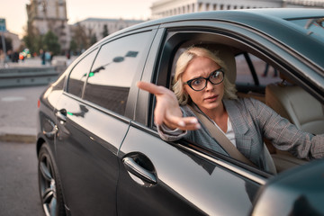 Troubles on the road. Portrait of angry business woman gesturing with hands and arguing with somebody while driving a car