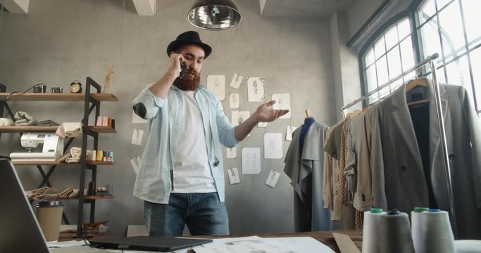 Cool hipster designer working in his office, talking or recording voice message on phone, making an order, customer service - fashion, small business concept 4k footage