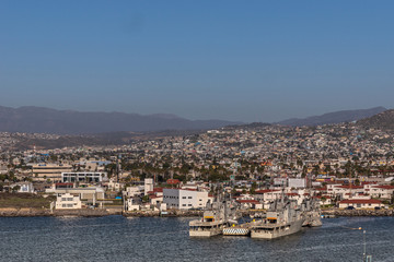Fototapeta na wymiar Ensenada, Mexico - January 17, 2012: Monasterio and Blanco gray navy vessels in port on blue bay water with cityscape in back under blue sky and hazy mountains.
