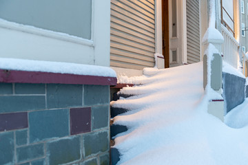 The steps of a vintage door filled with drifts of snow. The building is tan in color with white...