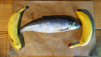 Close-up delicious salted herring and two yellow bananas on the old wooden background. Rustic style.